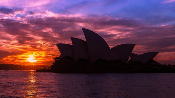 Tramonto sul Sydney Opera House con cielo colorato e riflessi sull'acqua.