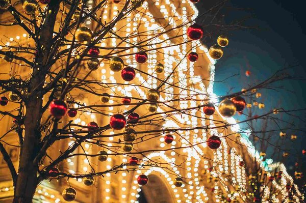 Decorazioni natalizie con luci e palline rosse e dorate su un albero, sfondo sfocato di un edificio illuminato.