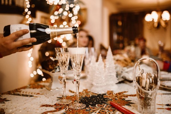 Champagne versato in bicchieri di cristallo su una tavola natalizia allestita per una cena pop-up, decorata con lucine.