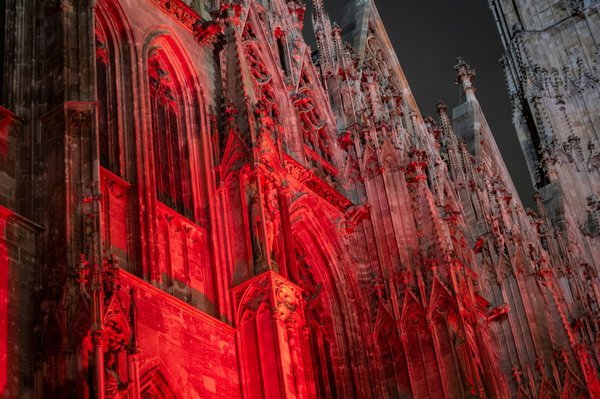 La facciata gotica di una cattedrale illuminata da una vivace luce rossa proiettata contro il cielo notturno.