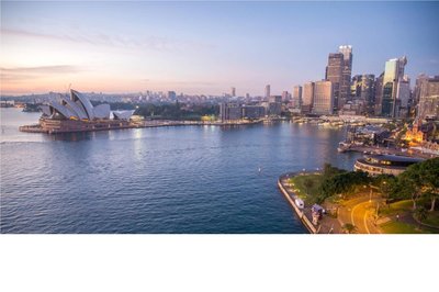 View of the Sydney Opera House and city skyline at sunset, with water and park in the foreground.