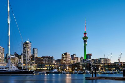 Auckland skyline with the illuminated Sky Tower and waterfront at dusk.