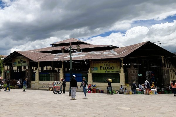 Mercato di San Pedro a Cusco con persone e bancarelle, cielo nuvoloso e architettura tradizionale.