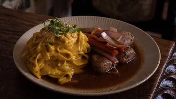Piatto tradizionale con tagliatelle cremose e carne in salsa, cucina autentica delle Ande a Cusco.