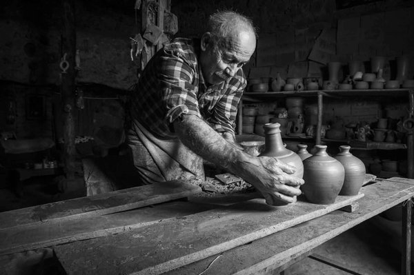 Artigiano che lavora in un laboratorio di ceramica tradizionale con vasi di argilla su un tavolo.
