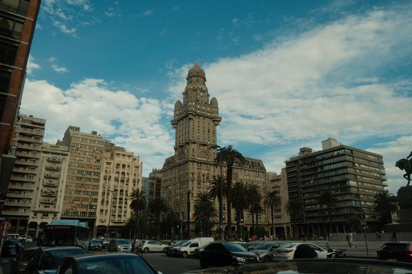 Vista del Palacio Salvo a Montevideo con palme e traffico in primo piano.