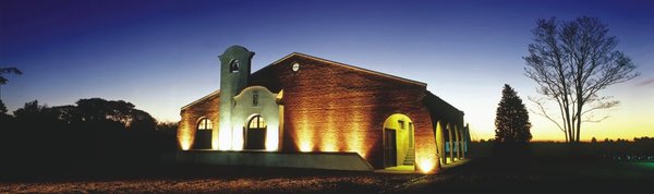 Illuminated facade of Bodega Bouza at sunset, Montevideo, with blue sky and trees in the background.