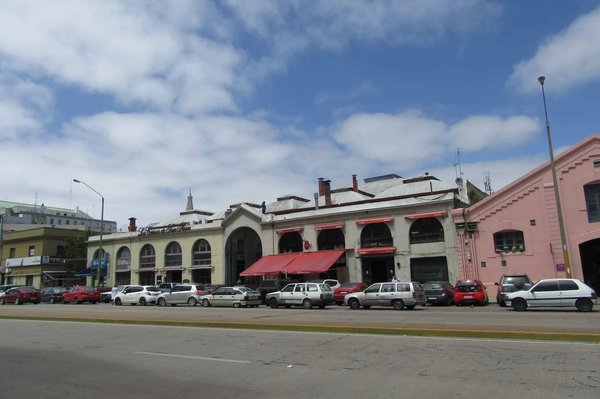 Facciata del Mercado del Puerto a Montevideo con auto parcheggiate e cielo parzialmente nuvoloso.